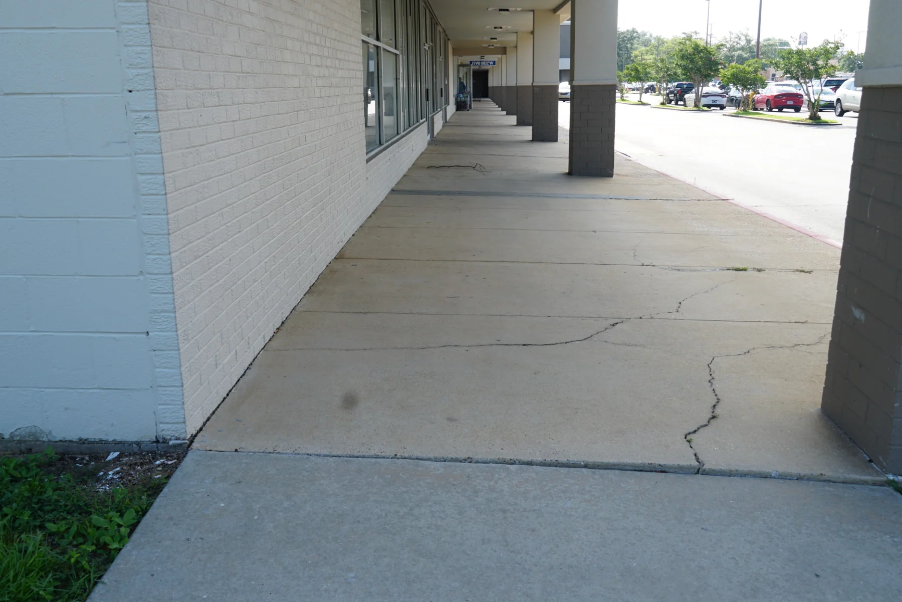 Original camera shot of the Pass Road shopping-center sidewalk leading toward Planet Fitness